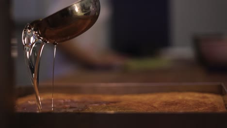 Cooking-spoon-pouring-hot-syrup-over-pot-with-baked-dessert,-slow-motion-shot