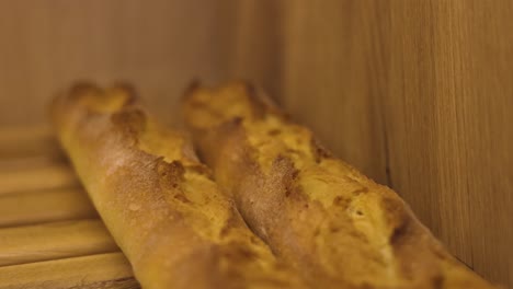 Baked-long-baguettes-with-golden-color-on-wooden-shelf-of-pastry-shop,-slow-motion-shot