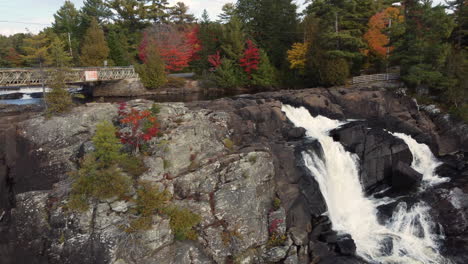 Panning-shot-of-waterfalls-over-rocks-on-the-edge-of-a-forest-covered-in-fall-colors