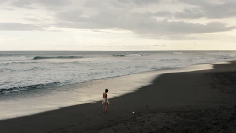 Woman-Walking-On-The-Beach-In-El-Paredon,-Guatemala-At-Sunset---aerial-drone-shot