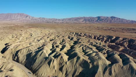 Aerial-Landscape-Drone-Flying-Over-Hilly-Arroyo-Tapiado-Mud-Caves-Towards-Mountains-on-Hot,-Dry,-Sunny-Day-with-Blue-Skies