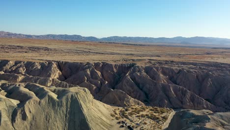 Aerial-Landscape-Drone-Slider-Shot-Flying-Over-Hills-Arroyo-Tapiado-Mud-Caves-Towards-Mountains-on-Hot,-Dry,-Sunny-Day-with-Blue-Skies