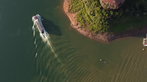 Drone-straight-down-shot-tourist-ferry-boat-cruising-on-Iguazu-River-at-sunset---People-visiting-natural-Rainforest-in-South-America