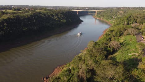 Drohnen-Panoramaaufnahme-Eines-Touristenboots,-Das-Während-Des-Goldenen-Sonnenuntergangs-An-Der-Iguazu-Flussgrenze-Zwischen-Argentinien-Und-Brasilien-Segelt