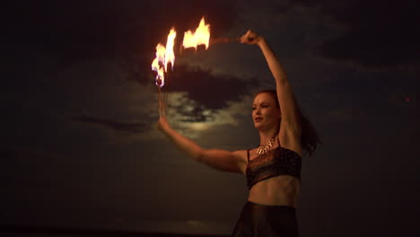 Woman-Dancing-With-Fire-Fans-Against-Cloudy-Full-Moon-Night-Sky,-Medium-Shot-Slowmo