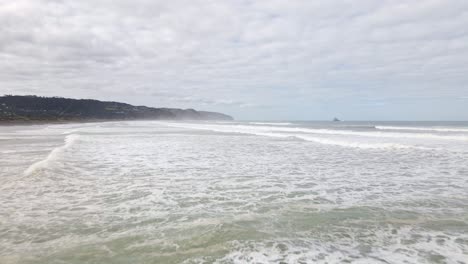 Niedrige-Luftaufnahme-über-Mehreren-Wellen,-Die-An-Der-Küste-Von-Muriwai-Beach,-Neuseeland,-Zusammenbrechen