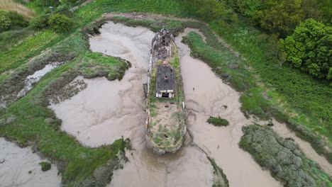 Aerial-view-of-a-Lighterboat-stuck-in-mud-at-Wat-Tyler-Country-Park,-cloudy-Basildon,-UK---tilt,-drone-shot