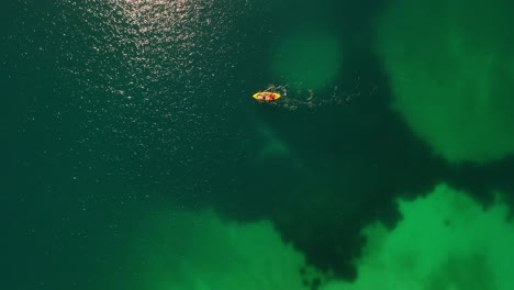 Aerial-looking-down-at-2-people-paddling-a-yellow-sea-kayak,-Albania