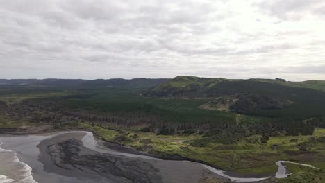 Aerial-push-in-shot-showing-Muriwai-beach-and-the-surrounding-forest,-New-Zealand