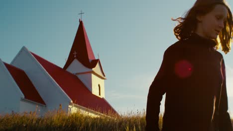 handheld-shot-of-a-girl-in-iceland-walking-in-front-of-a-church-at-sunset