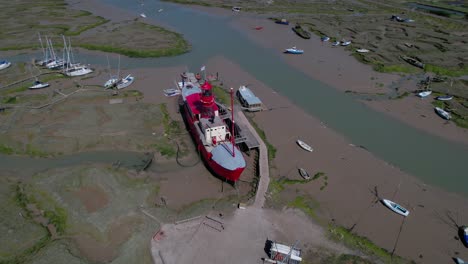 Aerial-view-around-a-lightship-stuck-in-mud-at-low-tide,-sunny-Tollesbury,-UK---circling,-drone-shot