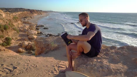 A-young-man-in-black-dress-and-sunglass-sitting-near-a-rocky-beach-with-ocean-in-the-background-at-Hadera,-Israel