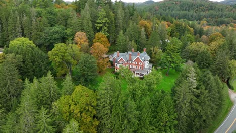 Rotational-aerial-drone-shot-of-brick-mansion-among-pine-forest-and-changing-fall-leaves