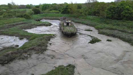 Aerial-view-around-a-mossy-Lighterboat-decaying-in-the-marsh-at-Wat-Tyler-Country-Park,-cloudy-Basildon,-UK---low,-orbit,-drone-shot