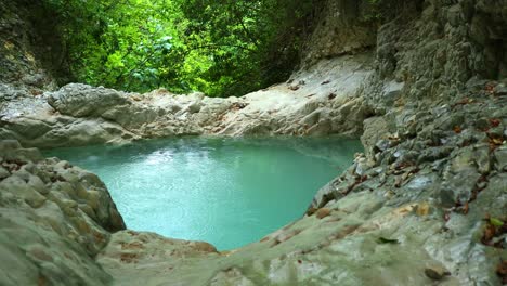 relaxing-nature-scene,-natural-swimming-pool-between-smooth-rocks-in-the-lush-and-peaceful-forest-in-a-windy-day