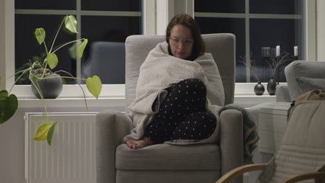 Energy-crisis-Europe,-Woman-with-blanket-freezing-indoors-checks-temperature-on-radiators