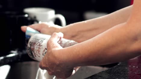 Woman's-hands-washing-glass-cup-with-sponge-and-soap-in-kitchen-sink-at-home,-slow-motion