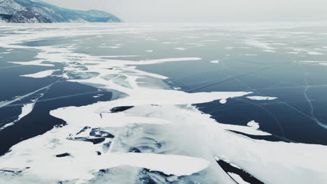 Aerial-frozen-lake-footage-landscape,-Lake-Baikal-in-winter-with-broken-blue-ice-at-Cape-Khoboy-on-Olkhon-Island-in-Siberia,-Russia,-Drone-shot
