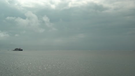 Timelapse-static-shot-of-a-sea-with-a-big-ship-and-isolated-small-boats-while-the-clouds-pass-by-quickly-in-calm-waters