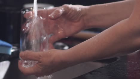 Close-up,-housewife-washing-glass-cup-under-kitchen-tap-at-home,-slow-motion
