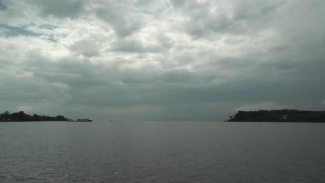 Time-lapse-wide-shot-of-a-lake-with-calm-waters-with-floating-boats-and-a-view-of-the-islands-with-forests-and-the-cloudy-sky