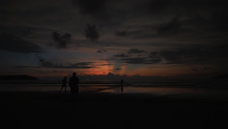 Static-time-lapse-shot-of-a-lake-with-calm-water-with-people-walking-on-the-shore-during-a-beautiful-sunset-with-passing-clouds