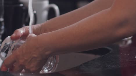 Woman's-hands-rinsing-glass-cup-under-kitchen-tap-at-home-in-slow-motion