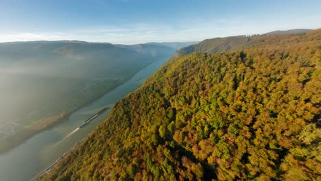 FPV-high-over-beautiful-Wachau-hills,-slowly-turning-towards-a-ship-on-peaceful-river-Danube,-glistening-in-the-autumn-sun