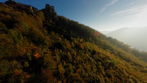 FPV-gliding-over-breathtaking,-colorful-forest,-ascending-over-medieval-Aggstein-before-diving-down-into-the-wachau-valley
