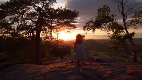 Shot-of-a-photographer-taking-pictures-at-sunset-with-her-camera-on-a-tripe-in-the-mountains