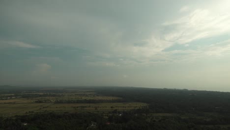 Static-timelapse-shot-of-a-wide-landscape-with-trees-and-large-fields-while-clouds-pass-by-on-the-horizon