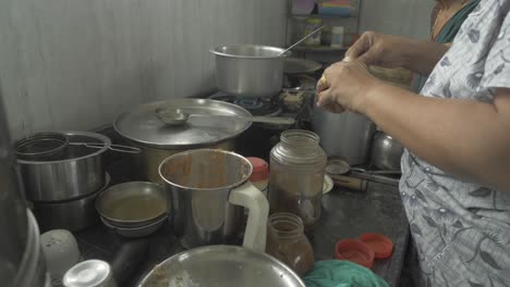Side-angle-of-a-middle-and-senior-aged-women-preparing-traditional-chicken-curry-and-bhakri-in-Indian-kitchen-using-cooking-gas-stove
