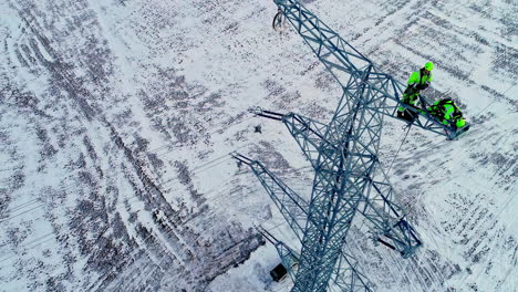 Aerial-tilt-up-shot-of-worker-installing-electricity-pylon-in-winter-landscape