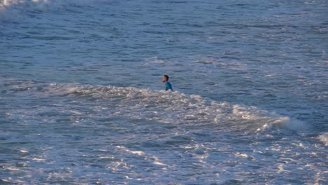 A-man-walking-into-the-ocean-to-surf-during-day-time-at-Haderah,-Israel