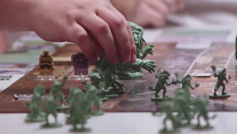 Hand-moving-green-characters-or-figures-on-desk-game,-closeup-view-of-next-turn