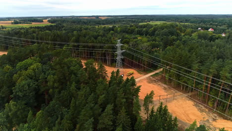 Aerial-drone-flight-over-woodland-with-construction-site-showing-worker-installing-new-transmission-towers