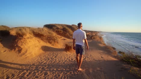 A-lonely-man-in-white-t-shirt-and-half-pant-walking-in-a-golden-beach-at-sunset-in-Haderah,-Israel