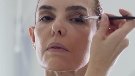 Middle-aged-woman-doing-makeup-with-brush-in-front-of-mirror-at-home