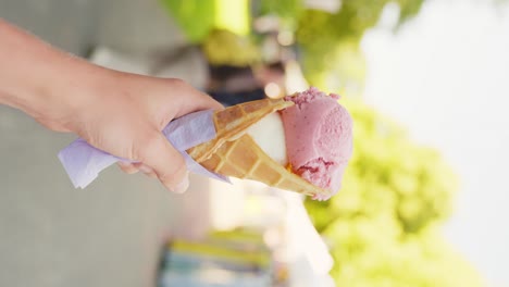 Vertical-clip-of-hand-holding-a-strawberry-and-vanilla-ice-cream-in-the-street