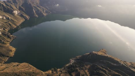 Paisaje-En-Quilotoa,-Lago-De-Cráter-Volcánico-En-Ecuador,-Drone-Aéreo-Sobre-El-Agua-Que-Calma-La-Vista-Panorámica-A-Lo-Largo-De-Los-Rayos-Del-Sol-De-La-Mañana