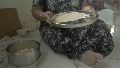 Wide-shot-of-an-Indian-woman-removing-stones-and-dirt-from-uncooked-rice-at-stainless-steel-plate-wearing-Indian-attire