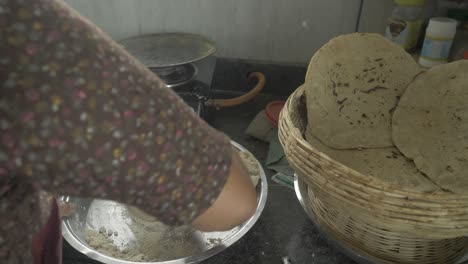 Over-the-shoulder-shot-of-a-senior-aged-woman-making-traditional-bhakri-in-Indian-kitchen-using-cooking-gas-stove