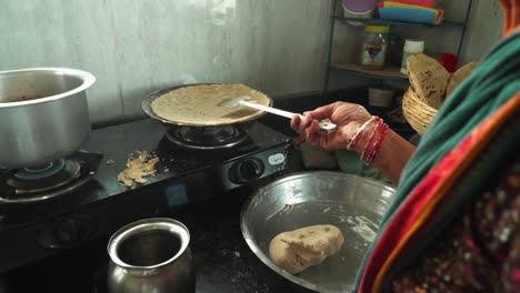 Seitenwinkelaufnahme-Einer-älteren-Frau,-Die-Traditionelles-Bhakri-Zubereitet-Und-Teig-In-Der-Küche-Des-Ländlichen-Indiens-Mit-Einem-Kochgasherd-Zubereitet