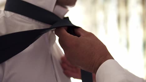 Slow-motion-handheld-close-up-shot-of-a-groom-getting-his-tie-tied-by-another-person-before-his-wedding-with-his-wife