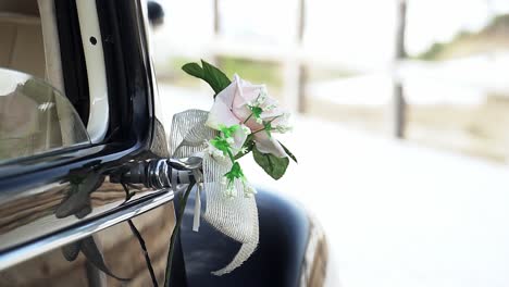 Slow-motion-handheld-panning-shot-of-a-rose-with-bow-attached-decoration-to-a-black-vintage-car-during-a-wedding-between-bride-and-groom