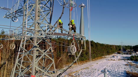 Aerial-drone-shot-of-electrical-workers-installing-electric-poles-along-rural-landscape-on-a-sunny-day-during-winter-time