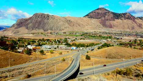 dolly-in-drone-shot-hyperlapse-of-Bridges-and-the-Highway-1-and-Yellowhead-Highway-5-in-Kamloops-BC-Canada-,-sunny-desert-city-with-cars-and-semi-trucks-driving-and-mount-paul-in-the-background