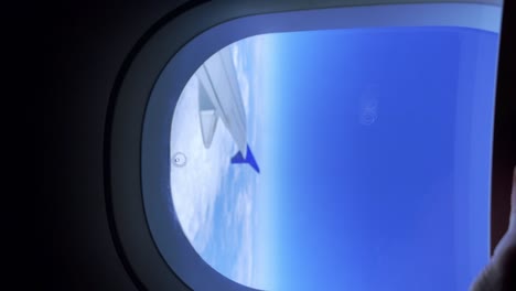 Close-up-of-passenger-man-hand-opening-airplane-window-blind-from-which-airplane-wing-and-clouds-can-be-seen