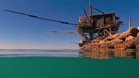 Split-underwater-view-of-trabocco-or-trabucco-at-Punta-Penna-beach-in-Costa-dei-Trabocchi-at-sunset,-Abruzzo-in-Italy