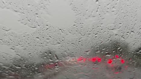 Strömender-Regen-über-Windschutzscheibe-Und-Rote-Verschwommene-Lichter-Des-Autoverkehrs-Im-Hintergrund-Mit-Wischer,-Der-Die-Windschutzscheibe-Von-Regentropfen-Reinigt